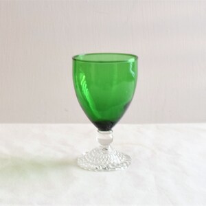 May include: A green glass goblet with a clear, textured base. The goblet is a traditional style with a wide bowl and a short stem.