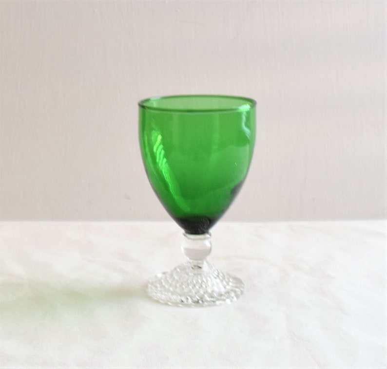 May include: A green glass goblet with a clear, textured base. The goblet is a traditional style with a wide bowl and a short stem.