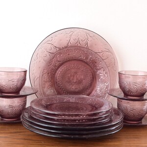 Pode incluir: Um conjunto de jantar vintage na cor lavanda. O conjunto inclui x&iacute;caras de ch&aacute;, pires e pratos, todos com um design floral em relevo. A disposi&ccedil;&atilde;o inclui pratos, x&iacute;caras e pires empilhados e um prato de servir grande.