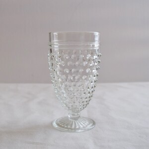 May include: A clear glass goblet with a textured, dimpled surface and a short stem. The goblet has a wide base and a rounded bowl.