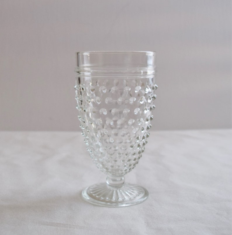 May include: A clear glass goblet with a textured, dimpled surface and a short stem. The goblet has a wide base and a rounded bowl.