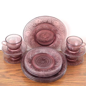 Pode incluir: Um conjunto de lou&ccedil;a de vidro roxo vintage, incluindo pratos, pires e x&iacute;caras de ch&aacute;. As pe&ccedil;as apresentam um design floral em relevo. O conjunto inclui v&aacute;rios pratos de tamanhos variados, pires e x&iacute;caras de ch&aacute;, todos em um tom roxo correspondente.