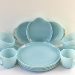 Puede incluir: Un juego de vajilla azul claro vintage, que incluye tazas, platillos y platos. El juego presenta una fuente para servir con borde festoneado y detalles dorados. La vajilla está dispuesta sobre una superficie blanca.