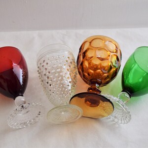 May include: Four different glass goblets, one red, one green, one clear with a textured surface, and one amber with a honeycomb pattern.