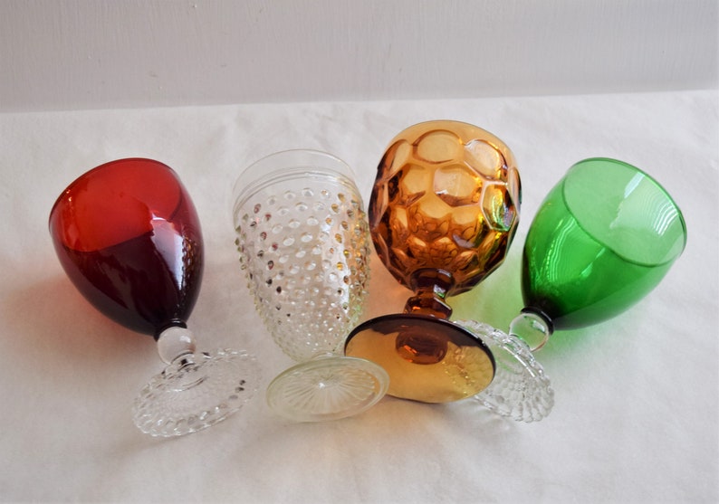 May include: Four different glass goblets, one red, one green, one clear with a textured surface, and one amber with a honeycomb pattern.