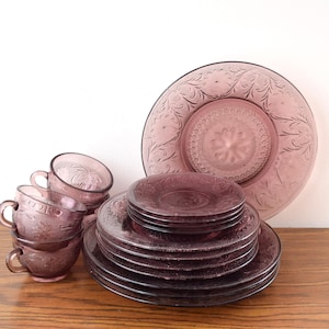 Pode incluir: Uma cole&ccedil;&atilde;o de lou&ccedil;as de vidro roxo vintage, incluindo x&iacute;caras de ch&aacute;, pires e pratos. Os pratos e x&iacute;caras apresentam um design floral em relevo. O conjunto inclui um prato grande, v&aacute;rios pratos menores e uma pilha de x&iacute;caras de ch&aacute;.
