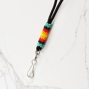 Peut inclure: Une lanière noire avec une section perlée. La section perlée présente un motif de perles turquoise, rouges, jaunes et noires. Un fermoir en métal argenté est attaché au bas de la lanière.