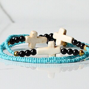 May include: A layered bracelet with turquoise and black beads and white cross charms.