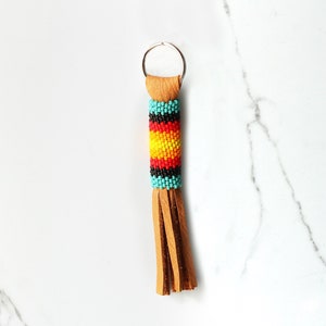 May include: A beaded keychain with a brown leather tassel. The beads are turquoise, black, yellow, red, and orange. The keychain has a silver key ring.