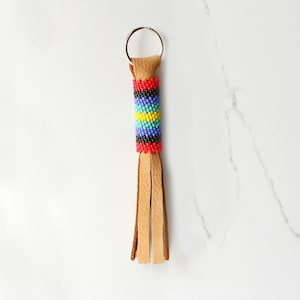May include: A brown leather keychain with a beaded tassel. The beads are red, blue, green, yellow, and black. The tassel is made of leather strips.