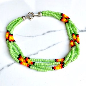 May include: A multi-strand bracelet with green, black, red, and yellow beads. The bracelet has a silver clasp.
