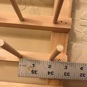 May include: A wooden dowel rod holder with 8ths of an inch markings on a ruler. The ruler is 4 inches long.