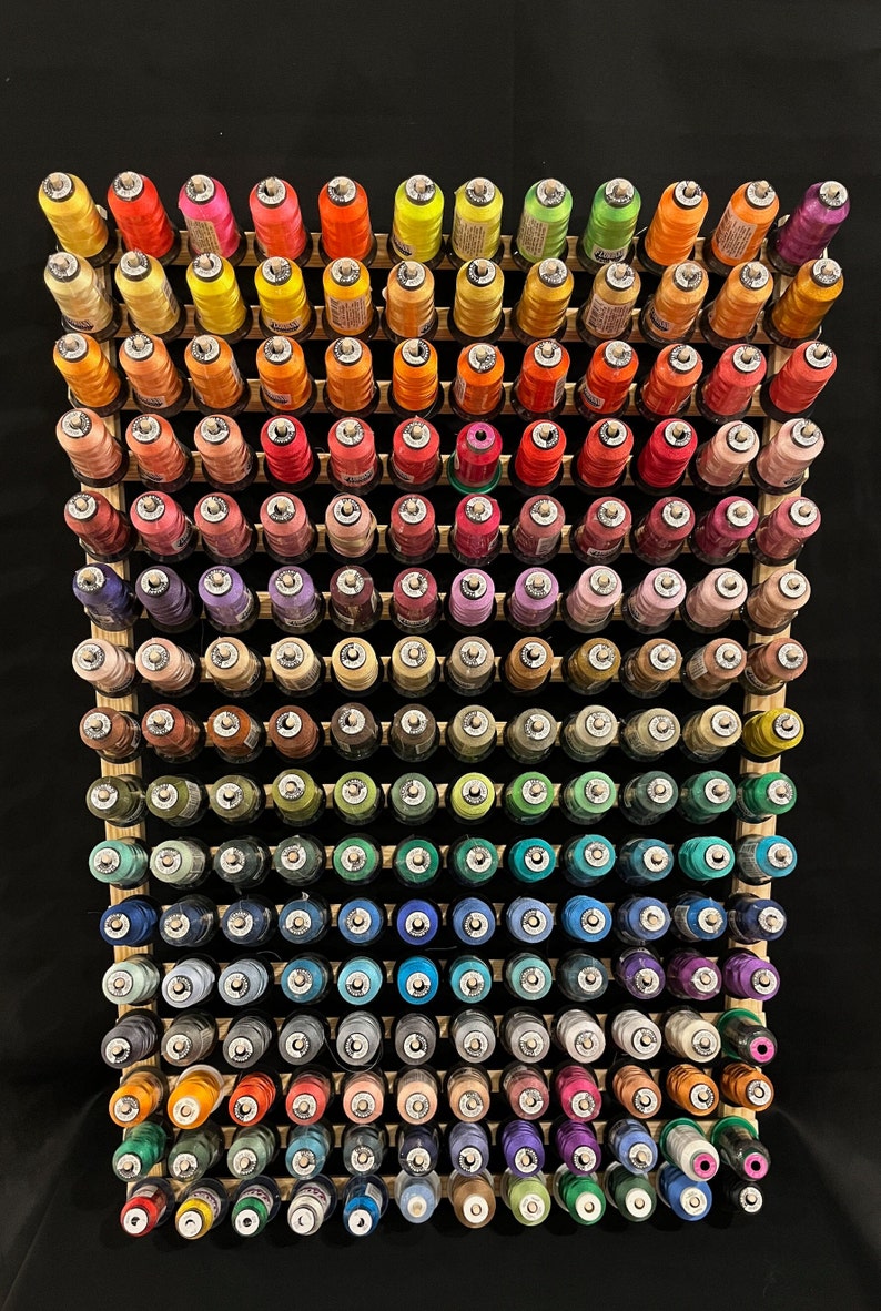 May include: A wooden rack with 10 rows of colorful thread spools. The spools are arranged in a rainbow pattern, with red, orange, yellow, green, blue, indigo, and violet threads.