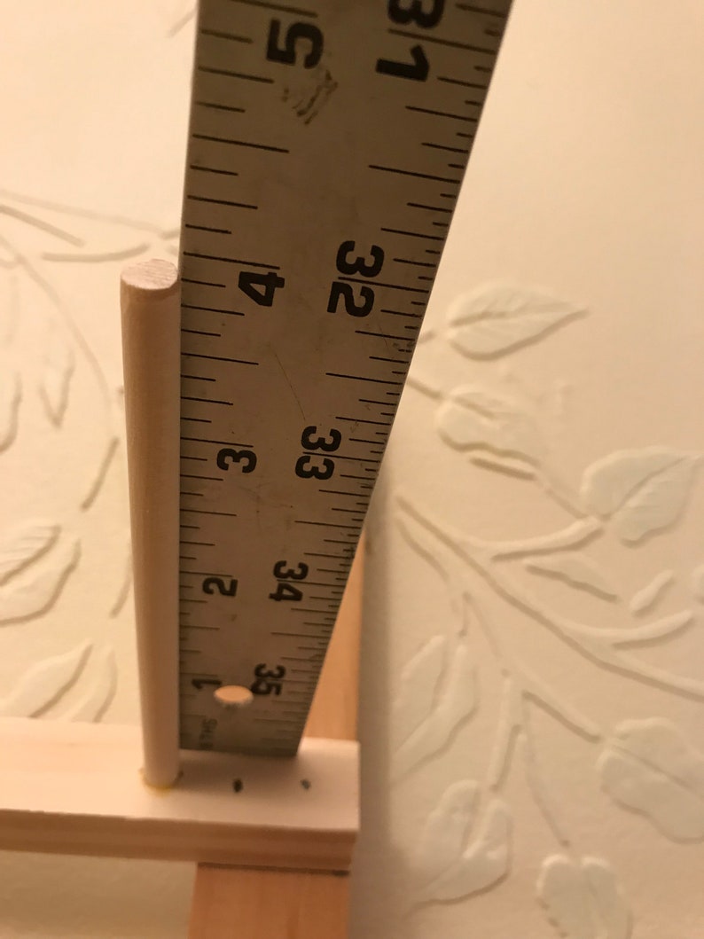 May include: A close-up of a wooden dowel rod measuring 3 1/2 inches in length, next to a ruler.
