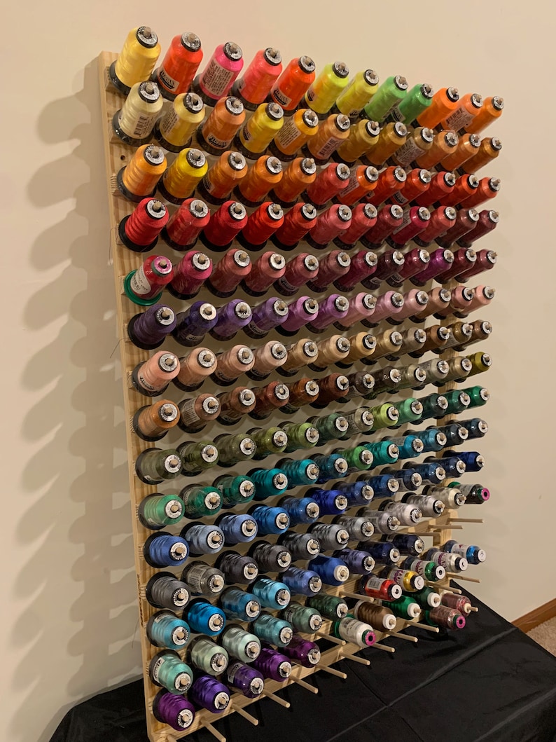 May include: A wooden thread rack with spools of thread in various colors, including red, orange, yellow, green, blue, purple, brown, and black.