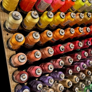 May include: A wooden rack filled with spools of colorful embroidery floss. The spools are arranged in rows and are labeled with the brand name "Floriani".