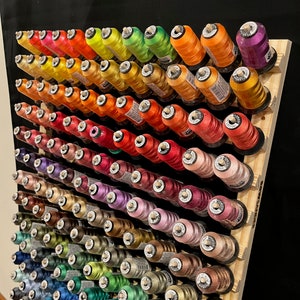 May include: A wooden embroidery thread rack with over 100 spools of colorful thread. The rack is labeled "Embroidery Thread Rack" and has a black background.
