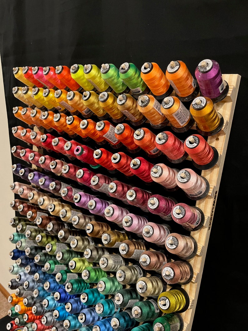 May include: A wooden embroidery thread rack with over 100 spools of colorful thread. The rack is labeled "Embroidery Thread Rack" and has a black background.