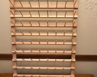 May include: A wooden spool rack with multiple rows of pegs for storing thread spools. The rack is made of natural wood and has a rustic look.