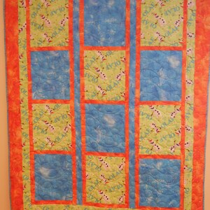Könnte beinhalten: Eine Steppdecke mit Patchwork-Muster, das ein blaues und grünes Muster mit dem Wort "Olaf" zeigt, das sich wiederholt. Die Steppdecke ist mit einem leuchtend orangenen Rand eingefasst.