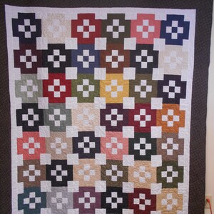 May include: A quilt made of various colored squares with a white cross pattern in each square. The quilt is framed with a brown border with white polka dots.
