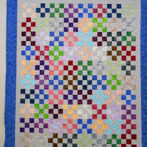 Może przedstawiać: Kolorowy koc z wzorem szachownicy. Koc wykonany jest z różnych tkanin o różnych wzorach i kolorach, w tym czerwonym, niebieskim, zielonym, fioletowym i brązowym. Koc jest obramowany niebieskim paskiem.