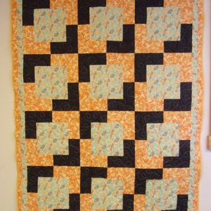 May include: A quilt with a geometric pattern of black and orange squares. The squares are arranged in a repeating pattern of L-shapes.