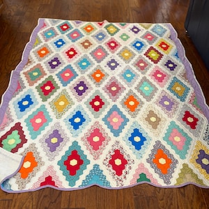 Könnte beinhalten: Eine bunte Patchwork-Decke mit Blumenmuster. Die Decke besteht aus verschiedenen Stoffen in den Farben Rosa, Blau, Grün, Gelb und Rot. Die Decke hat einen gewellten Rand und ist mit einer traditionellen Quilttechnik hergestellt.