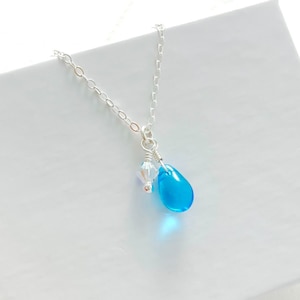 May include: A delicate silver necklace featuring a vibrant, teardrop-shaped, turquoise pendant. Accompanying the pendant is a small, clear crystal. The necklace is a simple, elegant piece of jewelry.