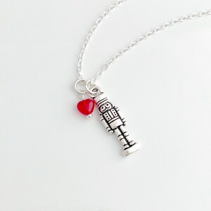 May include: Silver necklace with a red heart charm and a silver nutcracker charm.