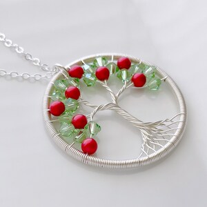 Op de afbeelding: Zilveren draad boom des levens ketting met rode en groene kralen. De ketting ligt op een witte achtergrond.