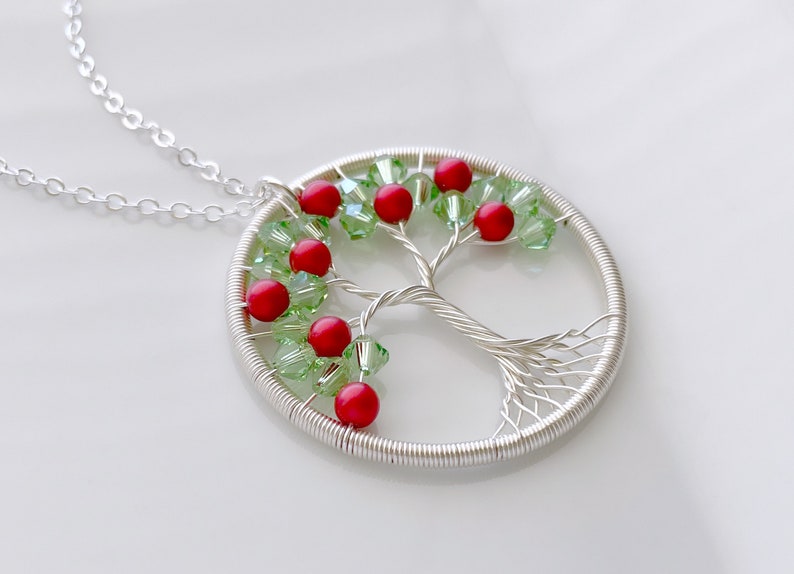 Op de afbeelding: Zilveren draad boom des levens ketting met rode en groene kralen. De ketting ligt op een witte achtergrond.