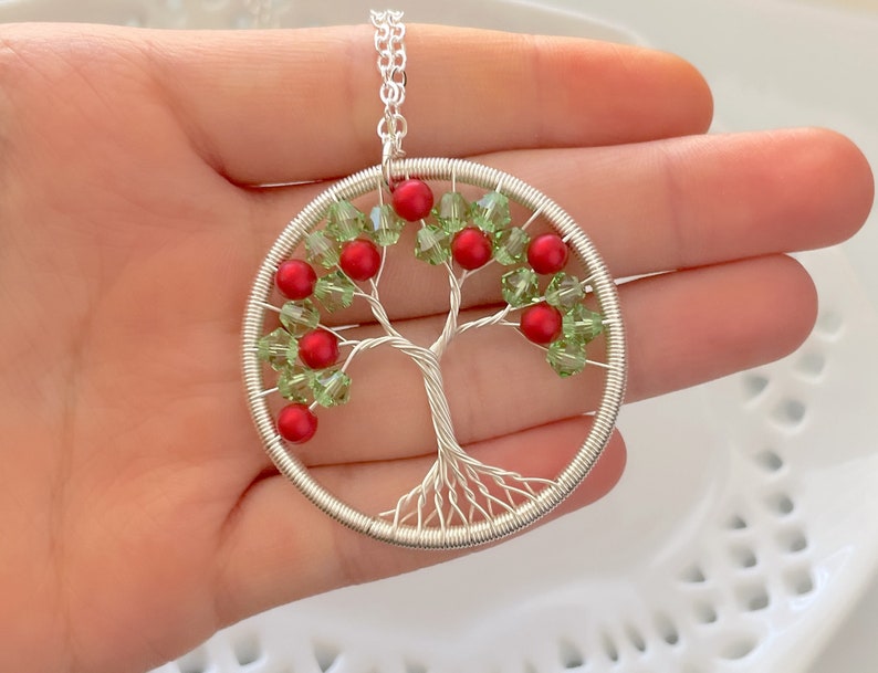 Op de afbeelding: Een zilveren draad gewikkelde boom des levens hanger ketting met rode en groene glazen kralen. De hanger is rond en hangt aan een zilveren ketting.