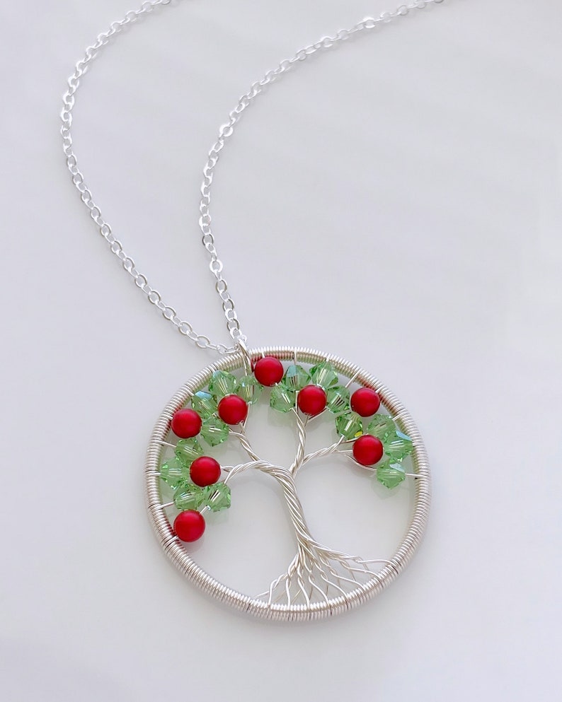 Op de afbeelding: Een zilveren ketting met een draadgewikkelde levensboomhanger. De hanger is versierd met rode en groene kristallen kralen.