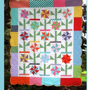 May include: A colorful quilt pattern called "Gracie's Garden" designed by Karen Bennett. The quilt features a white background with a repeating pattern of green stems, red, yellow, blue, and pink pinwheels, and a polka dot border.
