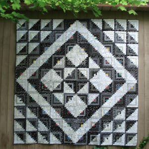 May include: A black and white quilt with a geometric pattern of triangles and squares. The quilt is made up of many small pieces of fabric sewn together.