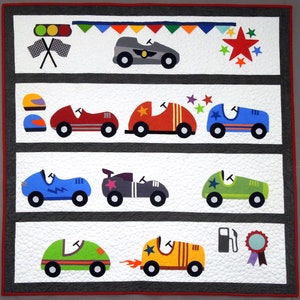 May include: A colorful quilt with a patchwork design featuring a variety of cars and a starburst pattern. The quilt is made with different fabrics and colors, including red, blue, green, yellow, and black. The cars are all different shapes and sizes, and some have stars on them.
