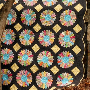 May include: A colorful quilt with a black background and gold diamond shapes. The quilt is made up of many different fabric scraps sewn together in a circular pattern.