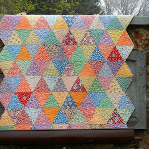 Könnte beinhalten: Ein farbenfroher Quilt aus Patchwork-Dreiecken in Orange-, Gelb-, Grün-, Blau-, Rosa- und Rottönen. Der Quilt besteht aus verschiedenen Stoffen mit Blumenmustern.