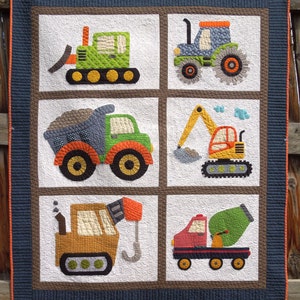 May include: A colourful quilt featuring six different construction vehicles, including a bulldozer, tractor, dumper truck, excavator, crane, and cement mixer. The quilt is made with a white background and brown, orange, green, yellow, and blue fabric.