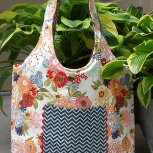 May include: A white tote bag with a floral print and a blue and white chevron patterned pocket. The bag has red trim around the pocket.
