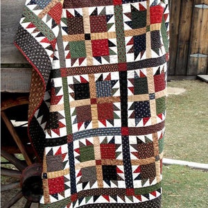 May include: A patchwork quilt with a geometric pattern in shades of red, green, brown, black, and white. The quilt is hanging on a wooden wagon wheel.