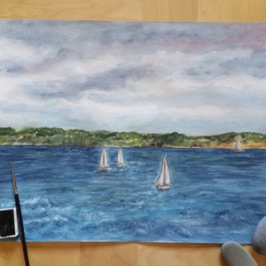 Könnte beinhalten: Aquarellmalerei einer Meereslandschaft mit vier Segelbooten auf einem blauen Gewässer. Der Himmel ist bewölkt und grau mit rosa und violetten Farbtönen. Der Horizont ist eine Linie grüner Bäume.