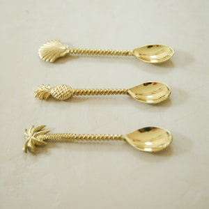 May include: Three gold-toned spoons with twisted handles and different decorative ends: a seashell, a pineapple, and a palm tree.