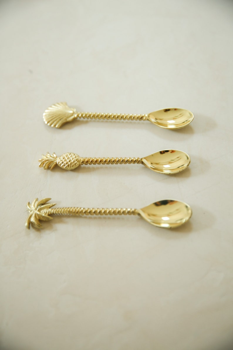 May include: Three gold-toned spoons with twisted handles and different decorative ends: a seashell, a pineapple, and a palm tree.