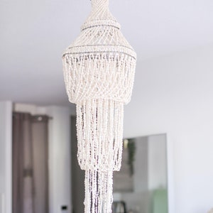 Peut inclure: Un lustre décoratif avec un design de coquillages blancs. Le luminaire est suspendu à un plafond blanc et présente plusieurs niveaux de coquillages en cascade, créant un élément d'éclairage élégant. Un élément de décoration intérieure unique.