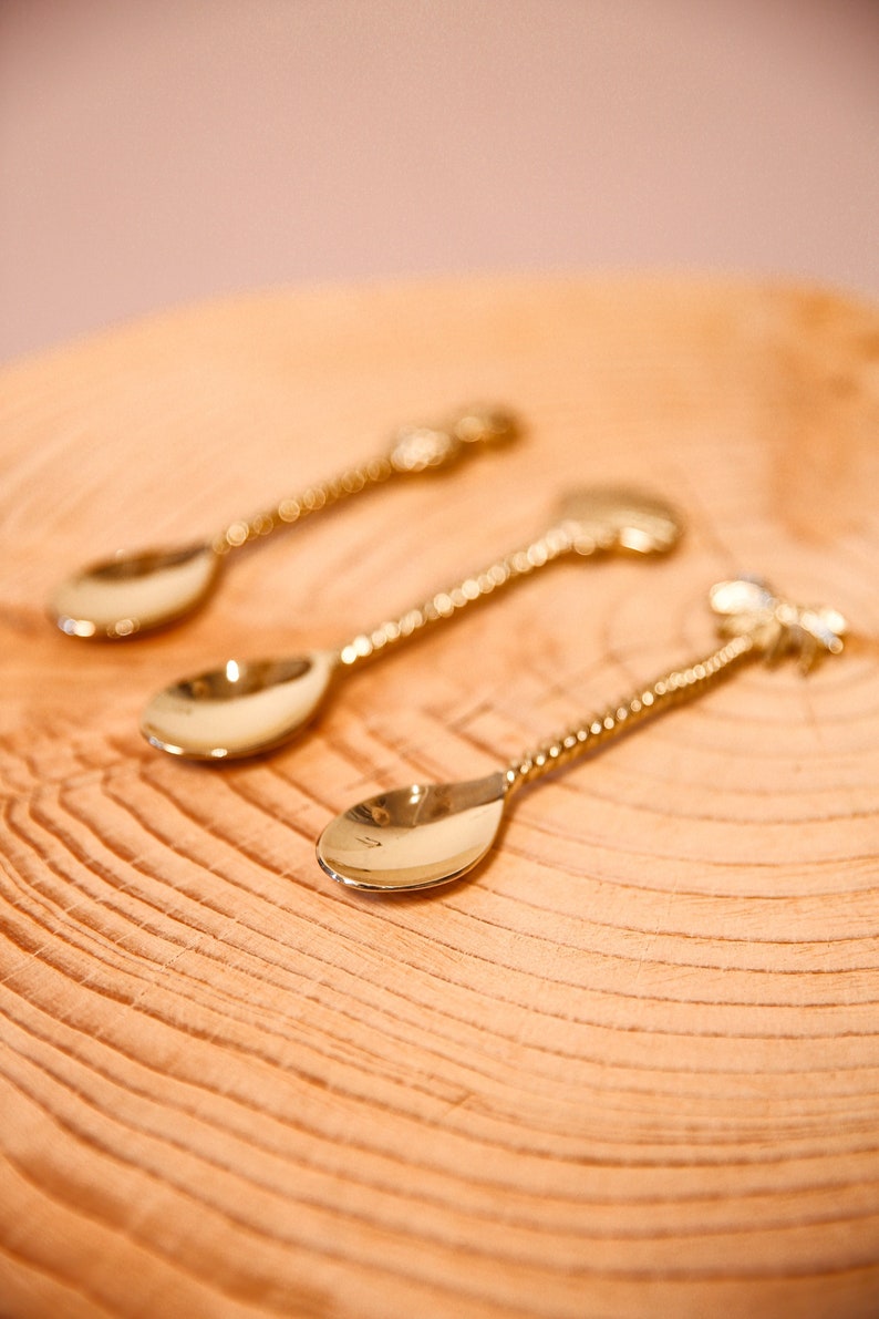 May include: Three gold-toned spoons with a twisted design. The spoons are on a wooden surface.