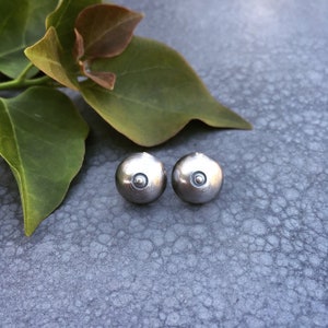 Puede incluir: Un par de pendientes de botón de plata con un pequeño círculo en el centro de cada pendiente.