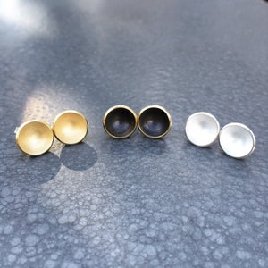 Puede incluir: Tres pares de pequeños pendientes redondos en forma de cúpula. Los pendientes están hechos de metal y están disponibles en oro, negro y plata.