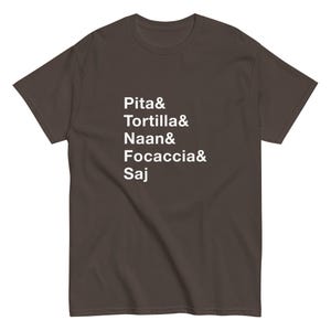 May include: A dark brown short-sleeved t-shirt featuring white text printed on the front. The text lists the following words vertically, each followed by an ampersand: Pita&, Tortilla&, Naan&, Focaccia&, and Saj. The shirt has a crew neckline.